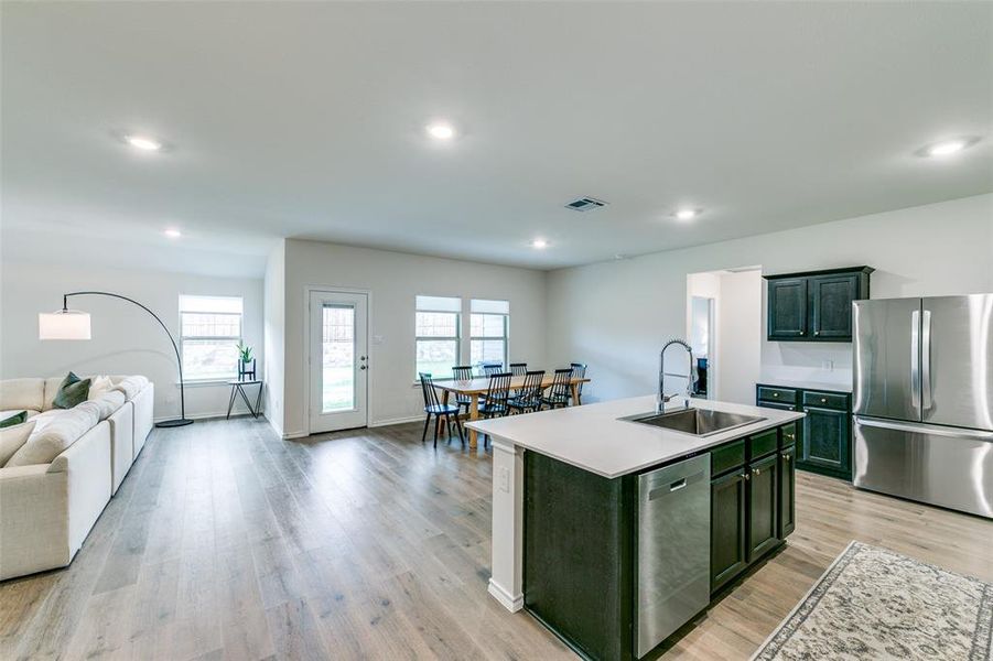 Kitchen featuring stainless steel appliances, sink, light wood-type flooring, and a kitchen island with sink