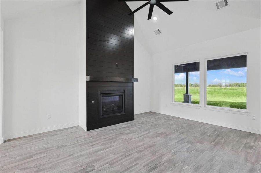 Unfurnished living room featuring high vaulted ceiling, ceiling fan, a large fireplace, and light hardwood / wood-style floors