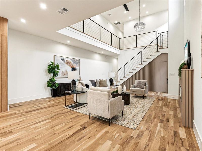 Living room with a high ceiling, a notable chandelier, and light hardwood / wood-style floors