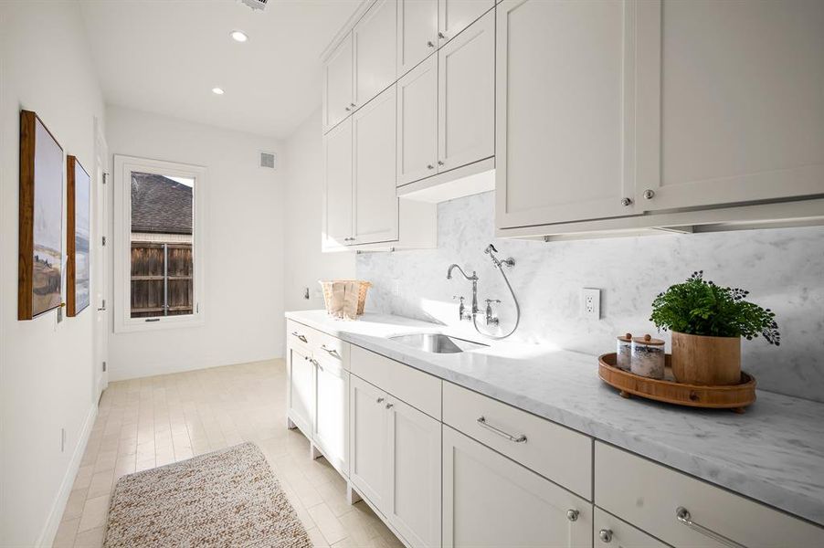 Kitchen featuring light stone countertops, decorative backsplash, sink, and white cabinets