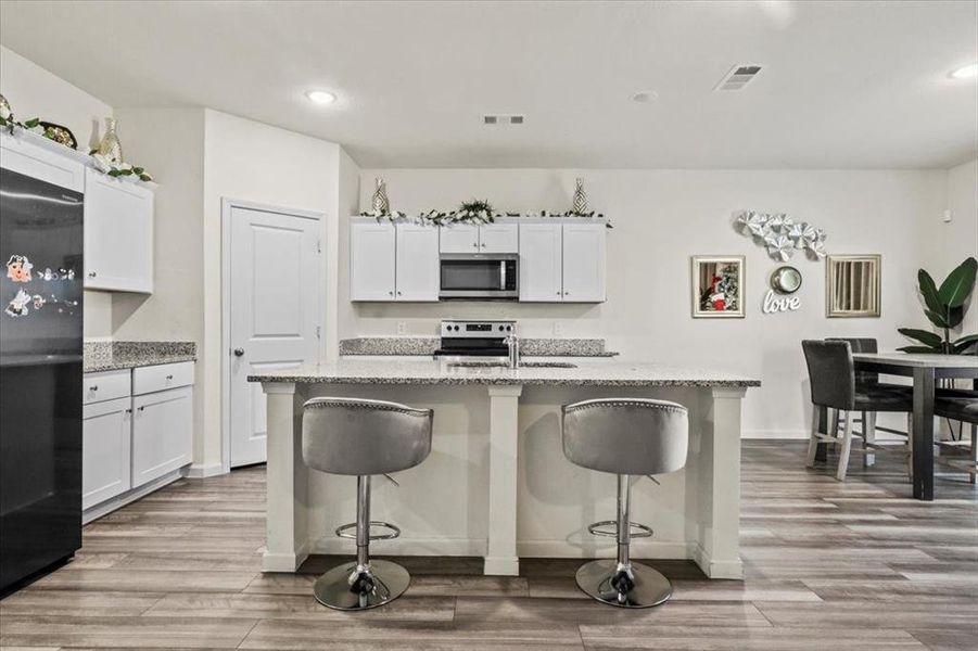 Kitchen with light hardwood / wood-style flooring, white cabinets, appliances with stainless steel finishes, and a kitchen island with sink