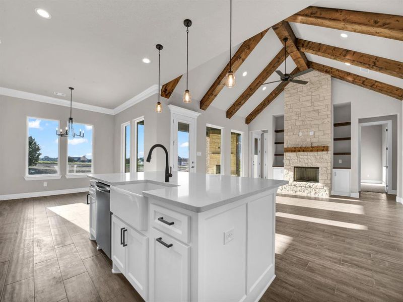 Kitchen with stainless steel dishwasher, pendant lighting, an island with sink, beamed ceiling, and a stone fireplace