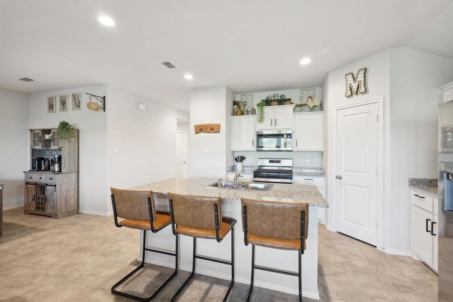 Kitchen with white cabinets, sink, a center island with sink, appliances with stainless steel finishes, and a kitchen bar