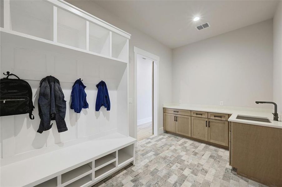 Oversized laundry area (directly off the garage) featuring abundant cabinet storage, large quartz counter space, laundry sink, designer tile work and hall-tree for organization and storage.