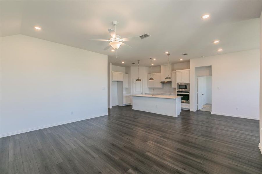 Unfurnished living room with vaulted ceiling, ceiling fan, and dark wood-type flooring