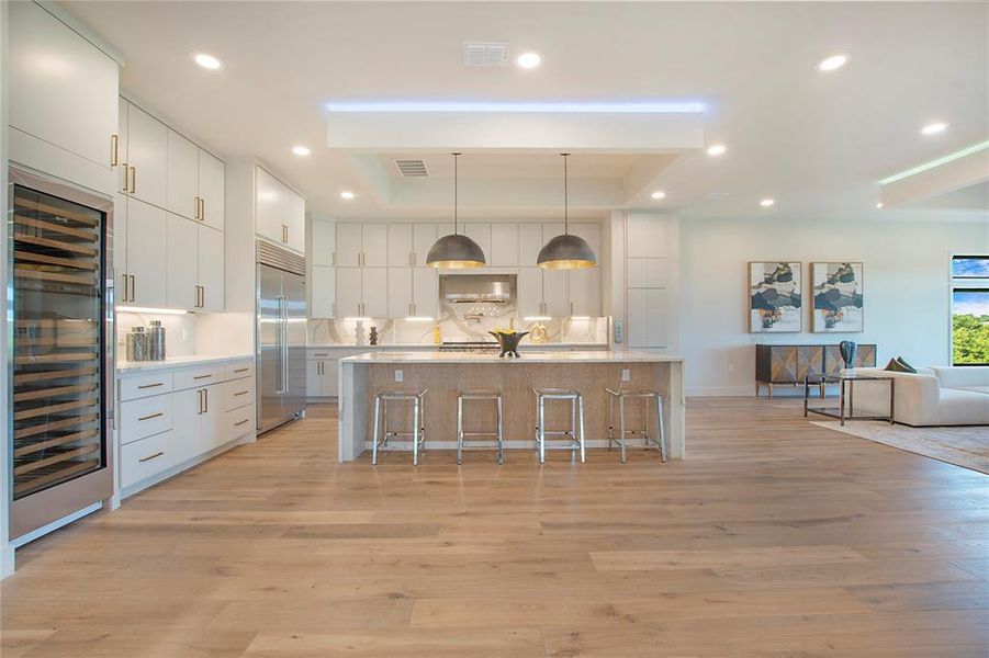 Kitchen with white cabinets, a breakfast bar, decorative light fixtures, stainless steel built in refrigerator, and light wood-type flooring