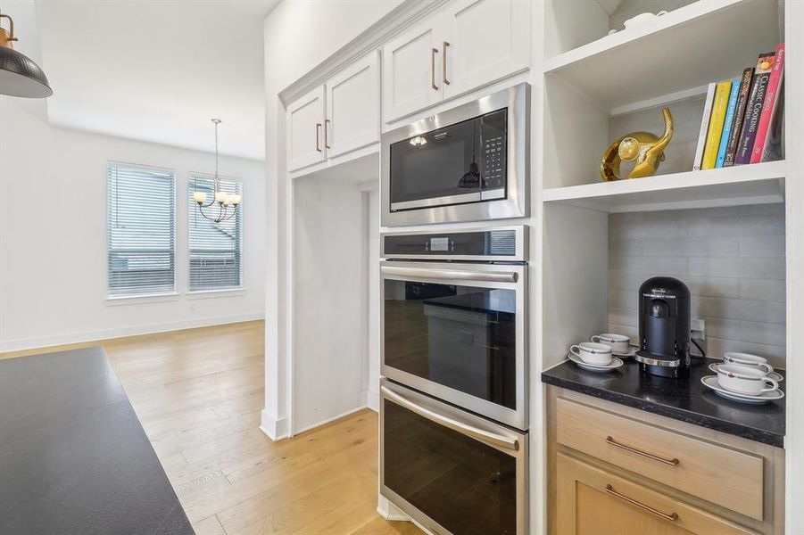 Kitchen featuring light wood-type flooring, backsplash, hanging light fixtures, white cabinetry, and appliances with stainless steel finishes