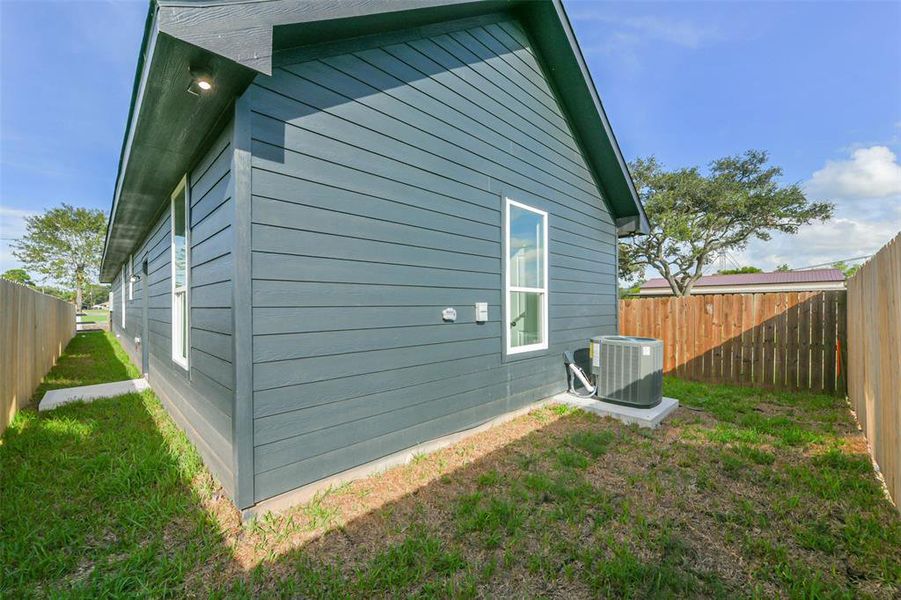 This is a side view of a house with gray siding and white trim, featuring a backyard with a wooden fence and a new HVAC unit.