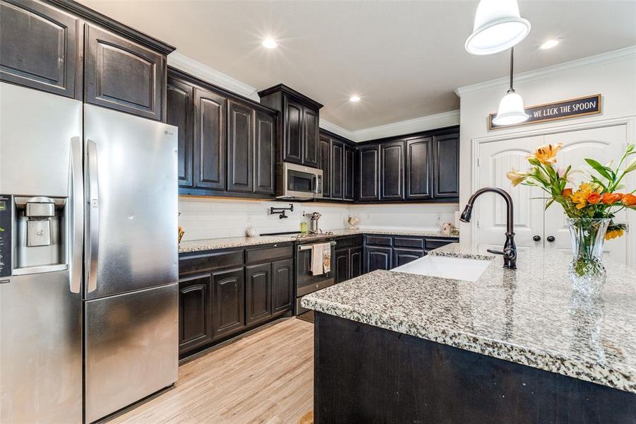 Kitchen featuring pendant lighting, stainless steel appliances, light hardwood / wood-style flooring, ornamental molding, and sink