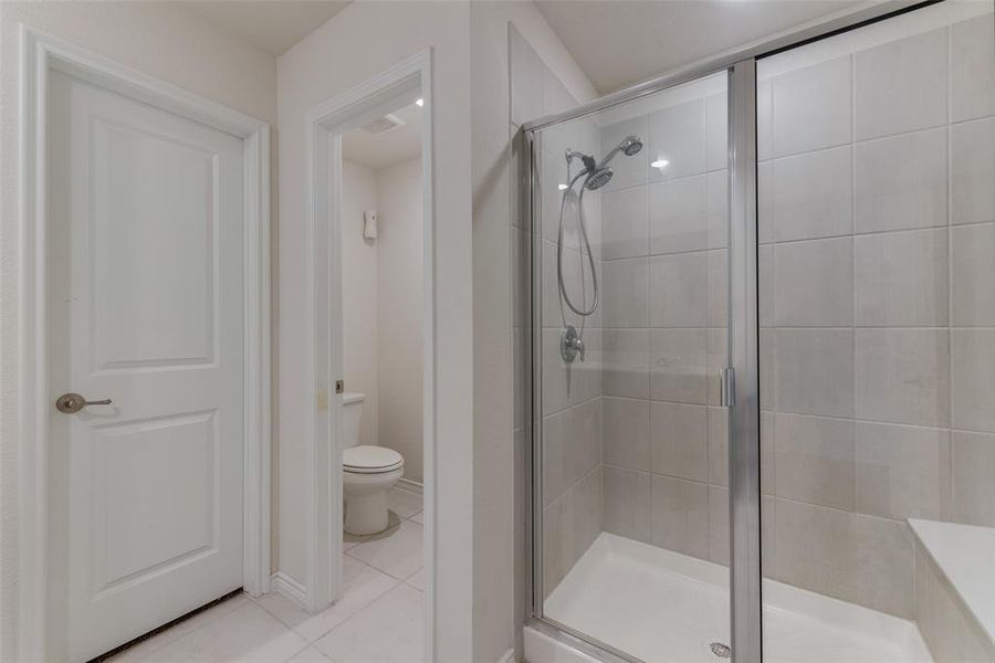 Bathroom featuring a shower with shower door, tile patterned floors, and toilet