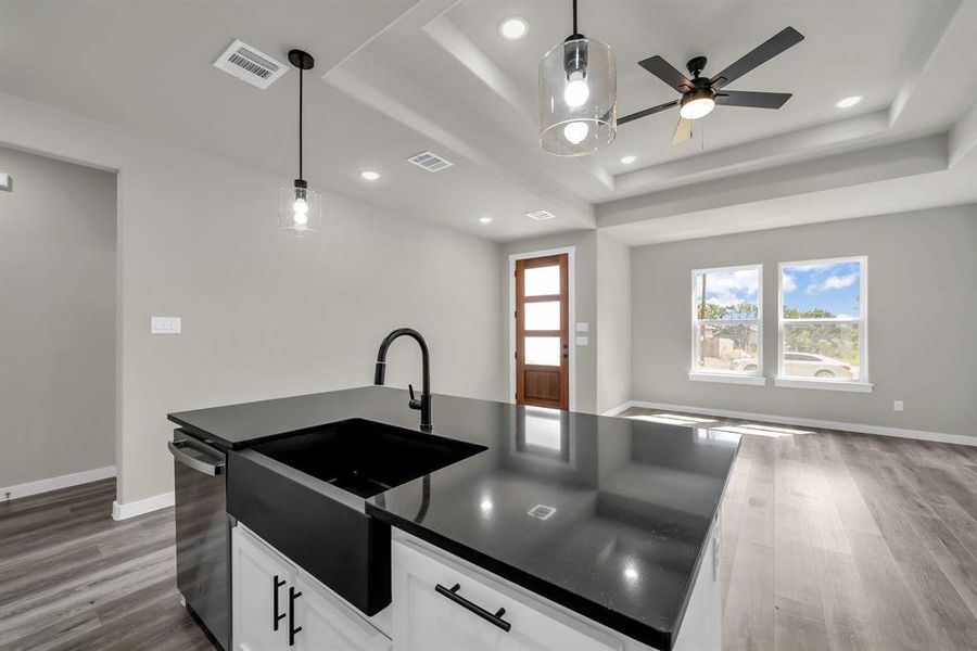 Kitchen with an island with sink, wood-type flooring, a raised ceiling, hanging light fixtures, and white cabinetry