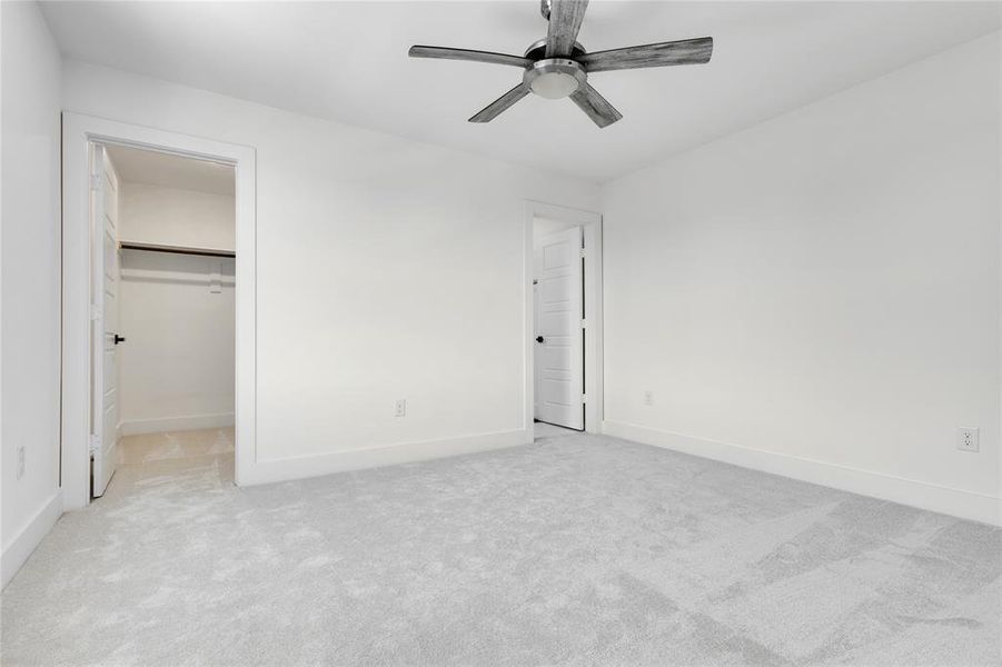 Unfurnished bedroom featuring light carpet, a walk in closet, a closet, and ceiling fan