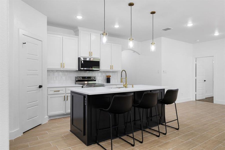 Kitchen with decorative light fixtures, stainless steel appliances, white cabinets, an island with sink, and backsplash