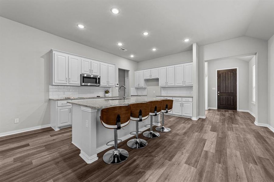 Kitchen featuring light wood-type flooring, white cabinets, light stone countertops, and an island with sink