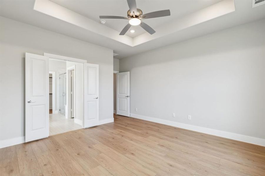 Unfurnished bedroom with a tray ceiling, light hardwood / wood-style floors, and ceiling fan