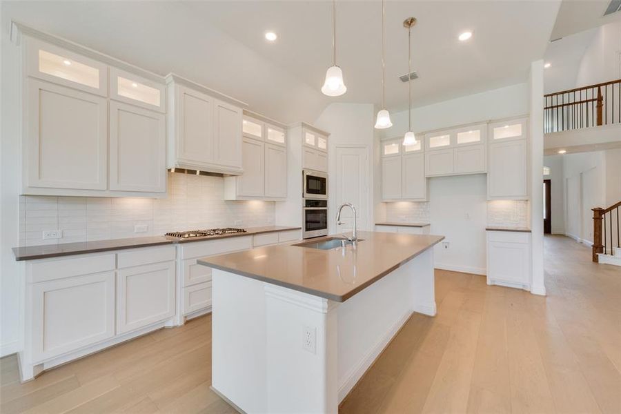 Kitchen featuring white cabinetry, light hardwood / wood-style flooring, backsplash, a kitchen island with sink, and appliances with stainless steel finishes