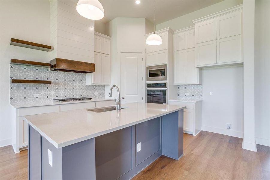 Kitchen with sink, white cabinetry, light wood-type flooring, and a kitchen island with sink