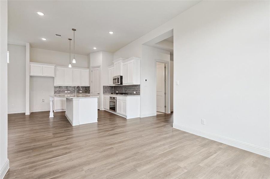 Kitchen with pendant lighting, white cabinetry, appliances with stainless steel finishes, and a kitchen island with sink