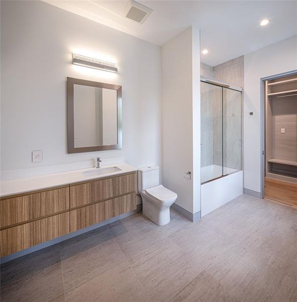 Ensuite secondary bedroom with custom built-in vanity, framed mirror, wall sconce and tub-shower