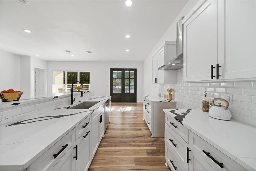 Kitchen with light hardwood / wood-style flooring, white cabinets, wall chimney range hood, sink, and decorative backsplash