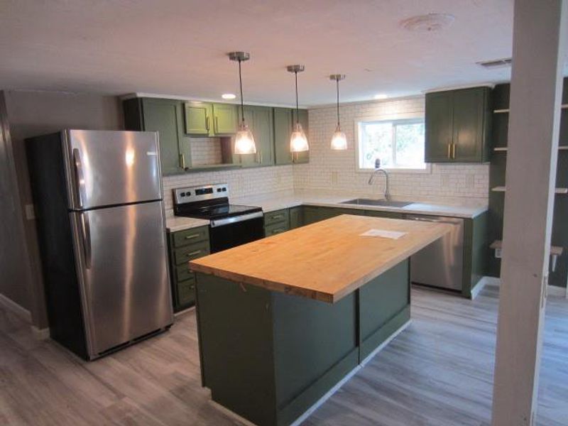 Kitchen featuring light wood-type flooring, butcher block countertops, green cabinetry, appliances with stainless steel finishes, and sink