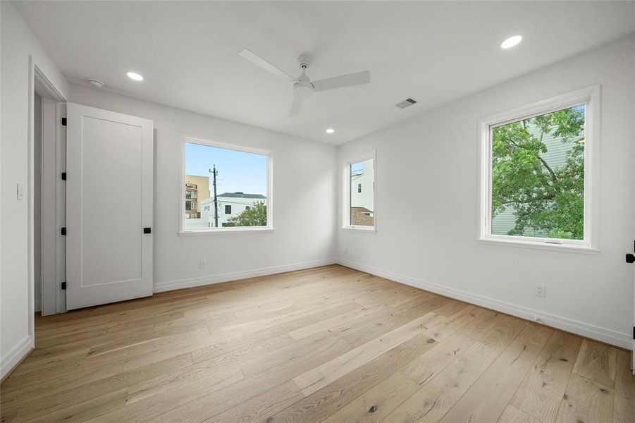 Bright, airy bedroom with hardwood floors, two windows allowing natural light, and a ceiling fan. Another bedroom with windows, full bathroom and walk-in closet.