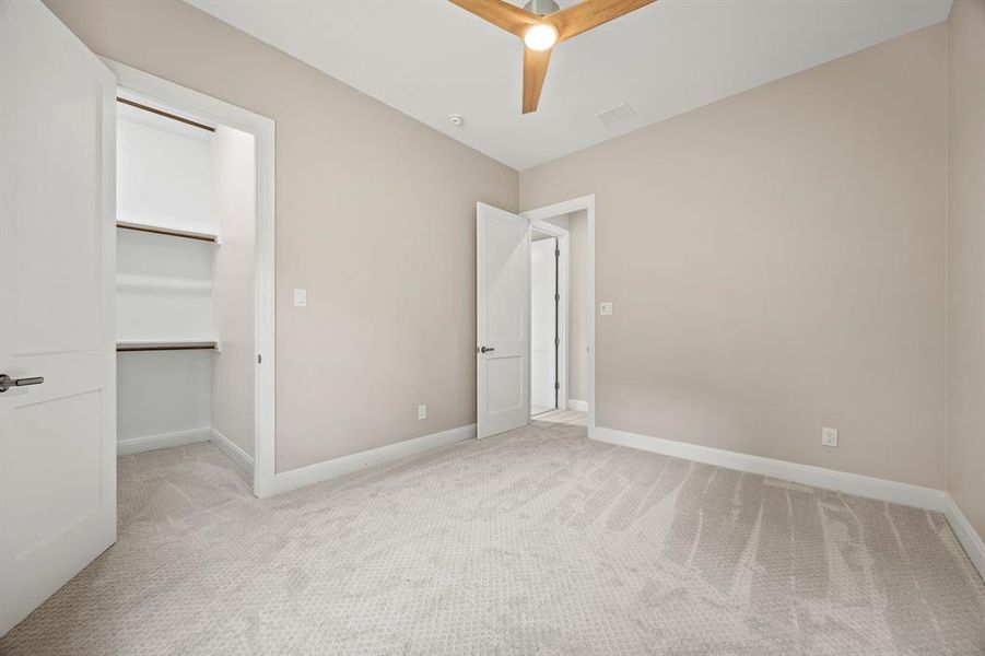 Unfurnished bedroom featuring ceiling fan, a walk in closet, a closet, and light colored carpet