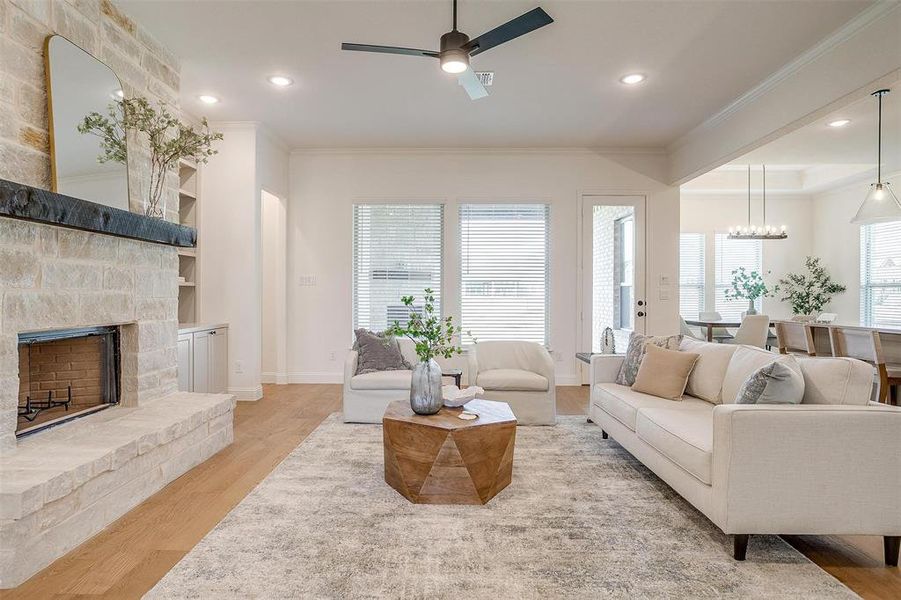 Living room featuring crown molding, ceiling fan with notable chandelier, a fireplace, and light wood-type flooring