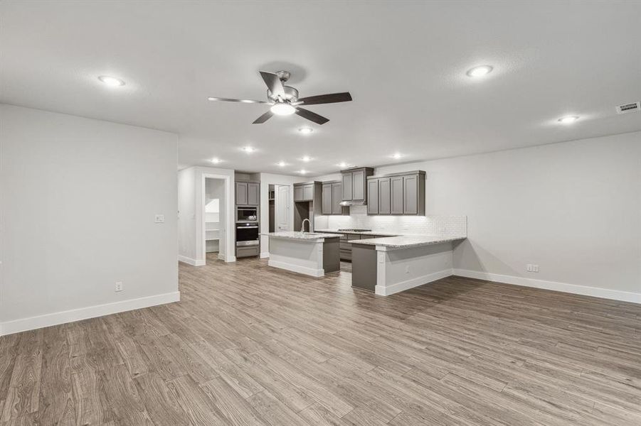 Kitchen featuring ceiling fan, decorative backsplash, hardwood / wood-style floors, a kitchen island, and a kitchen breakfast bar
