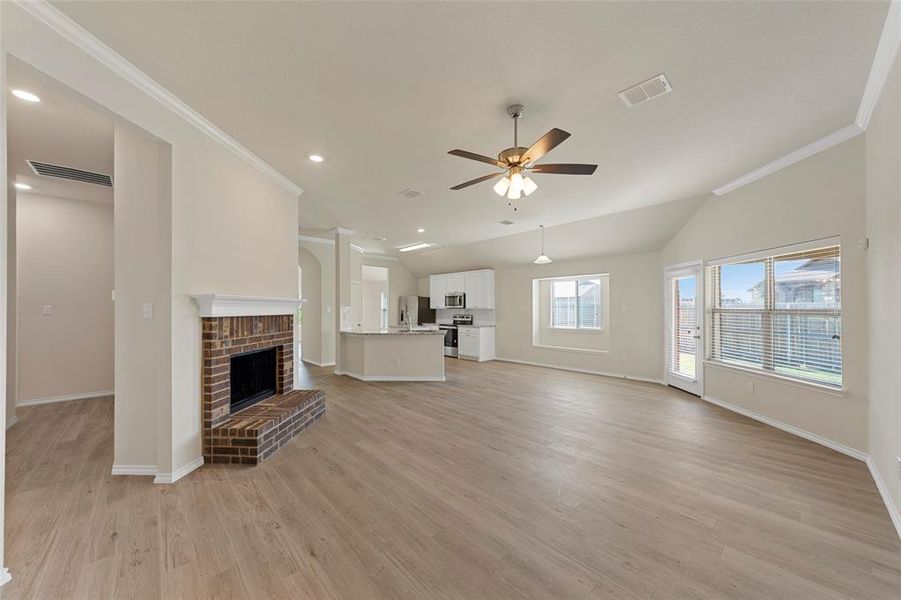 Unfurnished living room featuring light hardwood / wood-style flooring, ornamental molding, ceiling fan, and a fireplace