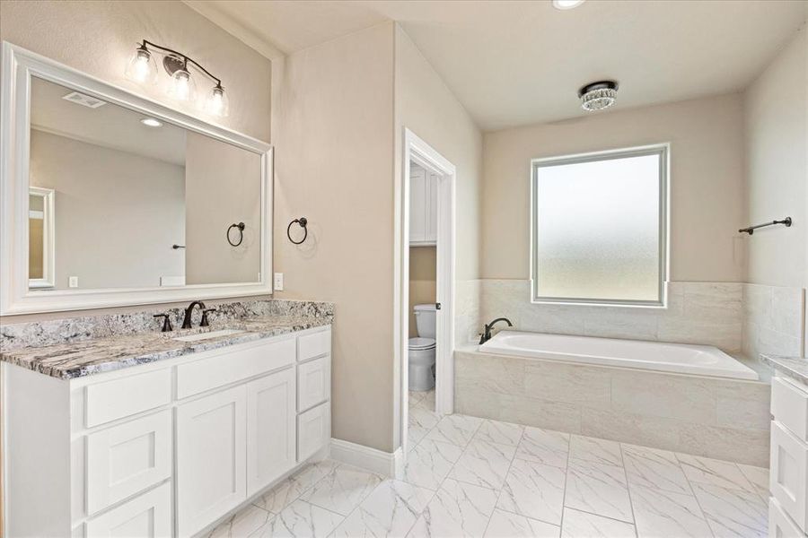 Bathroom featuring vanity, toilet, and tiled bath