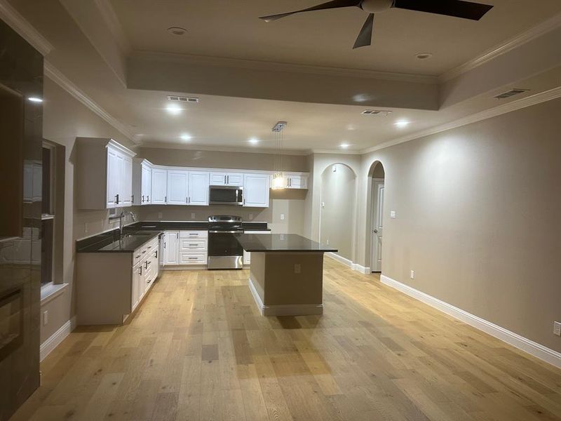 Kitchen with light hardwood / wood-style floors, white cabinetry, appliances with stainless steel finishes, ornamental molding, and ceiling fan