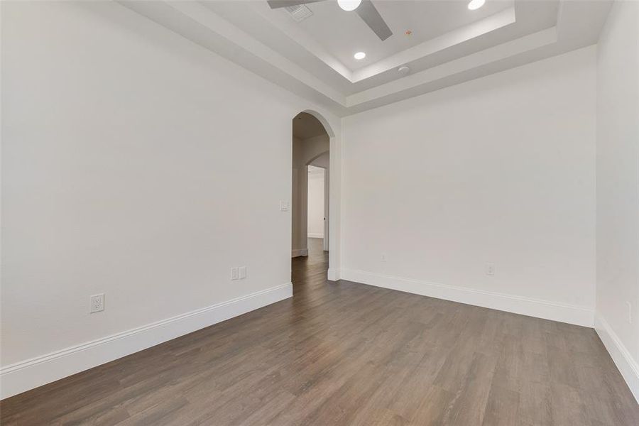 Empty room featuring ceiling fan, a tray ceiling, and wood-type flooring