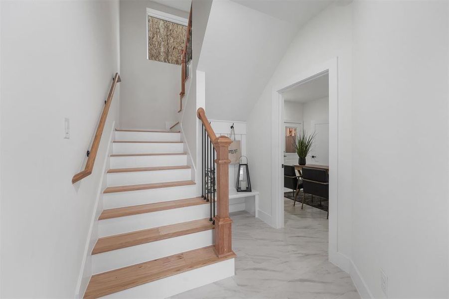 As you step into your bright, modern entryway with a staircase, you are greeted with stone tiled flooring, wooden custom handrails with white risers, leading to the upper second level. There's a glimpse into your well-lit secondary room with private en-suite bathroom.