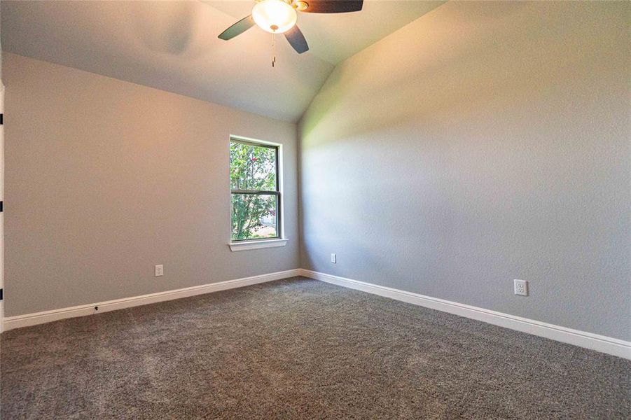 Spare room with ceiling fan, dark colored carpet, and vaulted ceiling