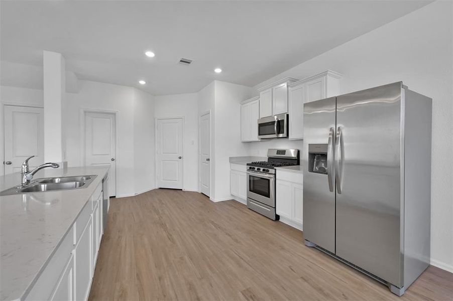 The view from the breakfast area to the kitchen, half bath and laundry room.  Quartz counters, long island/breakfast bar, 1-year-old stainless-steel appliances INCLUDING a side-by-side refrigerator