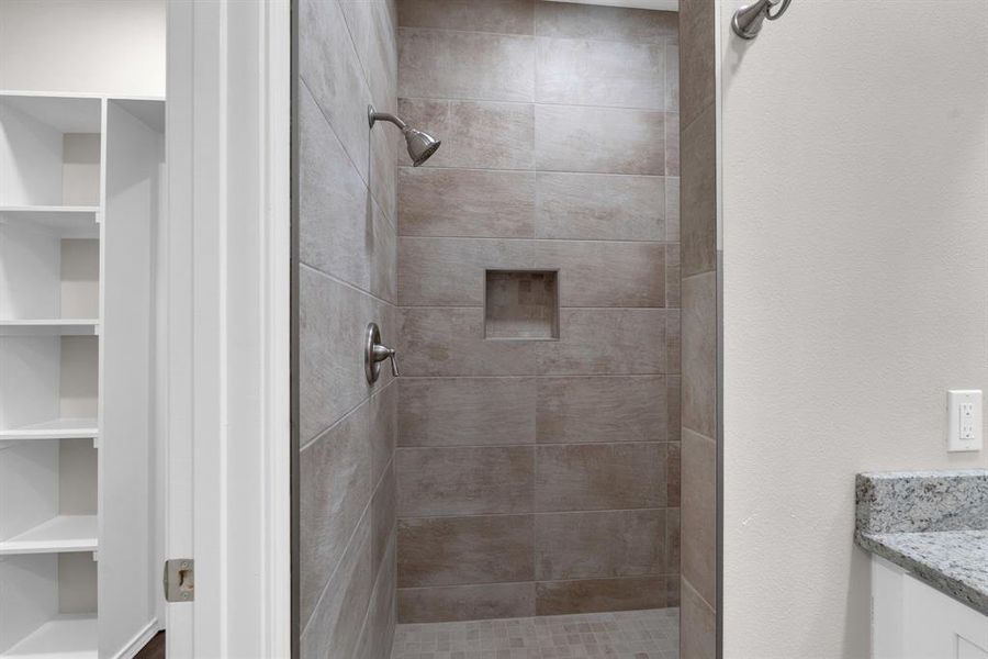 Bathroom featuring built in shelves, tiled shower, and vanity