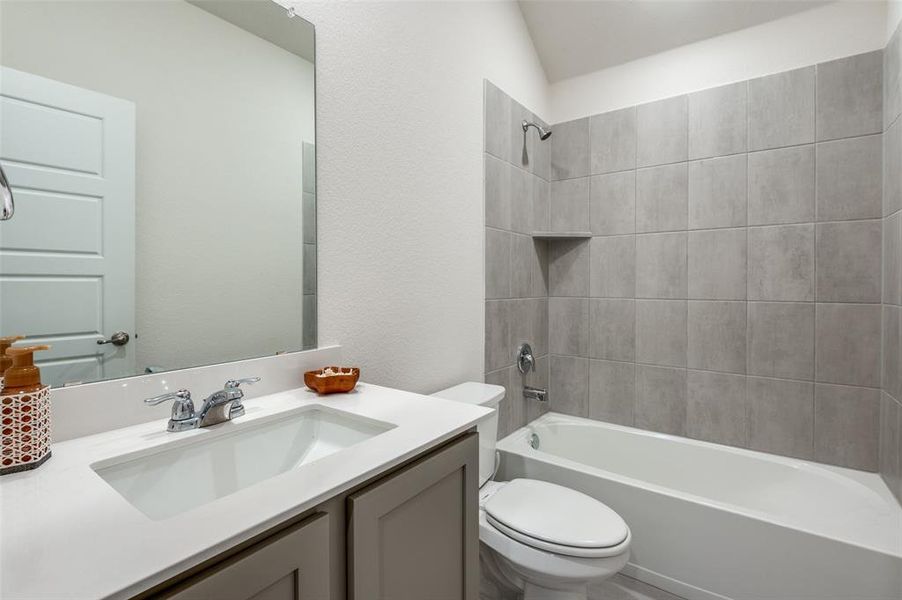 Full bathroom with vanity, tiled shower / bath, toilet, and vaulted ceiling