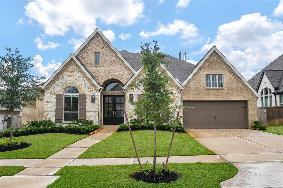 Modern single-story home featuring a brick and stone facade, a three-car garage, and well-manicured landscaping. The residence showcases a pitched roof and a welcoming entrance with a pathway leading to a stately front door.