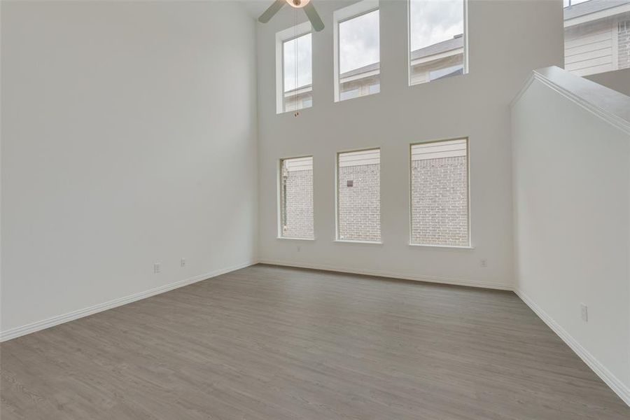 Unfurnished living room with ceiling fan, light hardwood / wood-style flooring, and a high ceiling