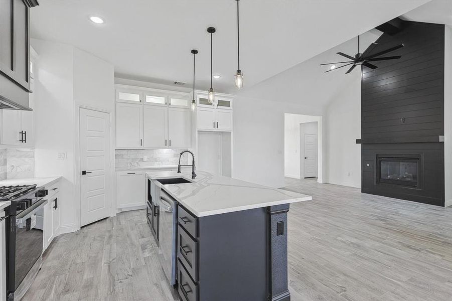 Kitchen with light stone counters, white cabinets, an island with sink, sink, and appliances with stainless steel finishes