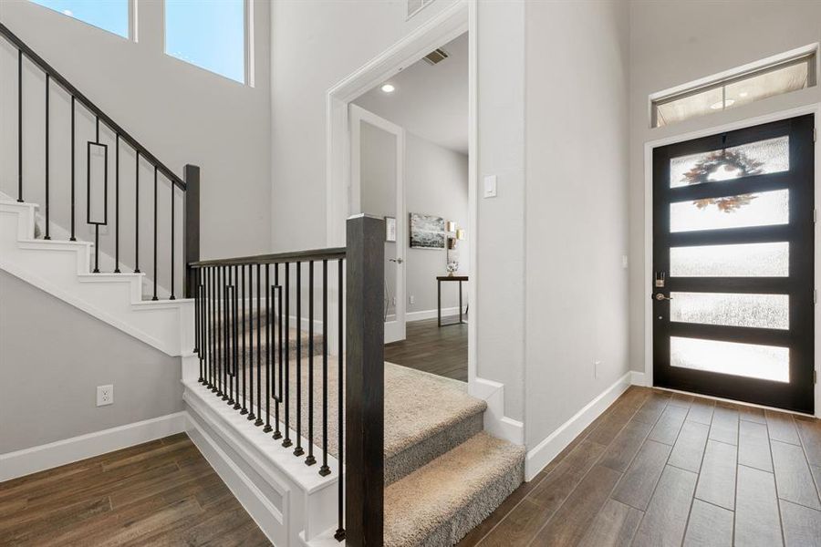 Step into a beautifully designed foyer that seamlessly connects to a versatile home office. The modern front door allows light to flow through, complementing the open staircase with elegant iron railings. Just off the entry, the office space offers privacy and functionality, with easy access from the main hallway, perfect for remote work or quiet study. The sophisticated flooring and neutral palette create a welcoming atmosphere for both work and relaxation.