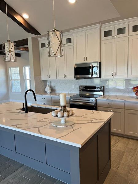 Kitchen featuring white cabinets, decorative backsplash, appliances with stainless steel finishes, decorative light fixtures, and light stone countertops