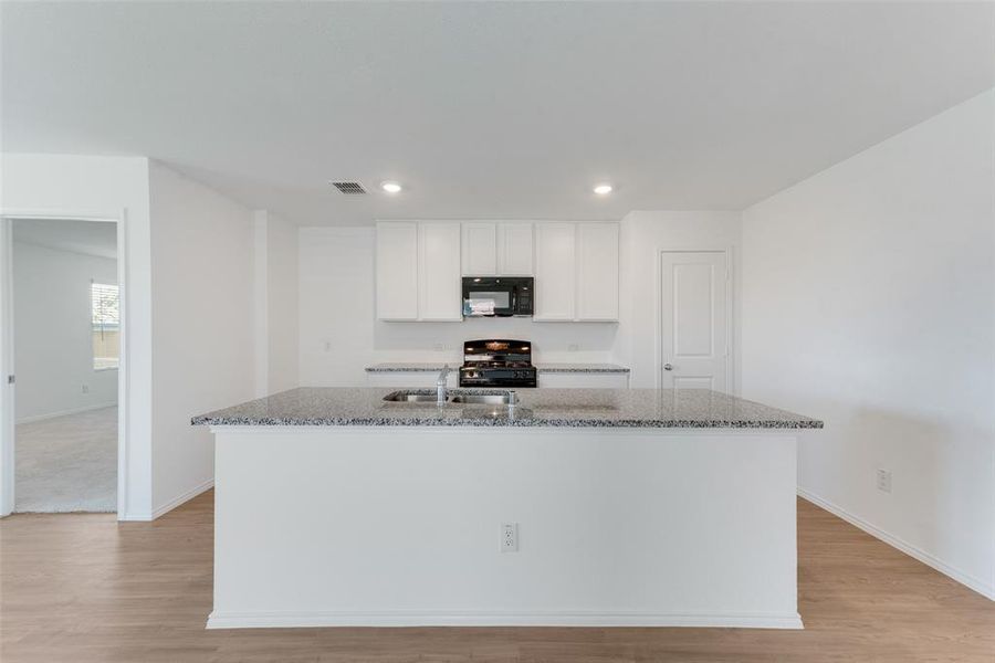 Kitchen featuring stone counters, black appliances, a kitchen island with sink, and white cabinetry