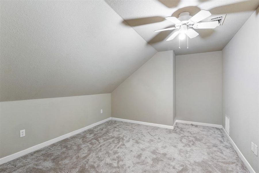 Additional upstairs living space featuring light carpet, ceiling fan, and a vauled ceiling