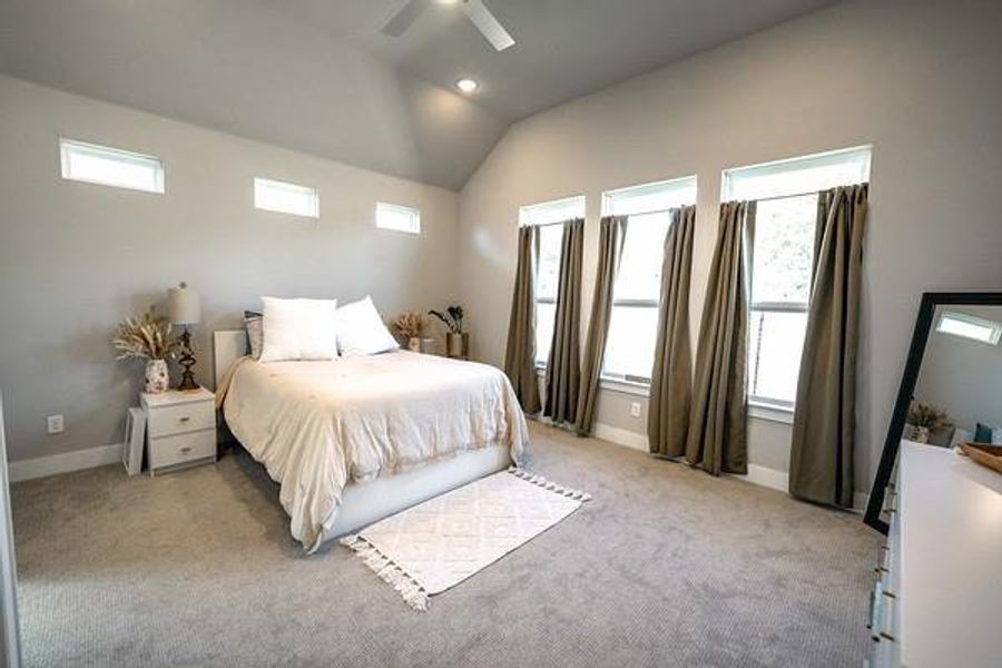 Carpeted bedroom featuring vaulted ceiling, multiple windows, and ceiling fan