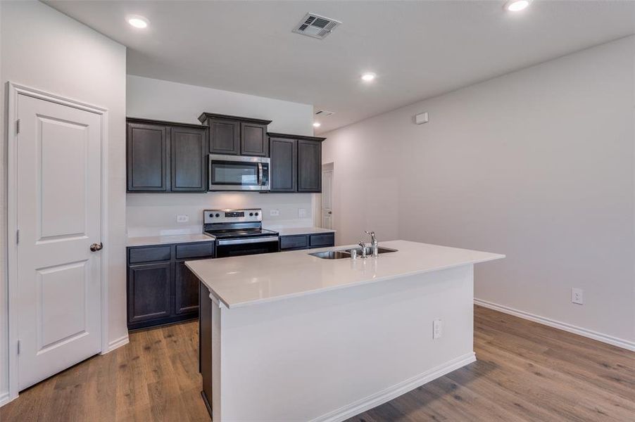 Kitchen with hardwood / wood-style floors, a kitchen island with sink, and stainless steel appliances