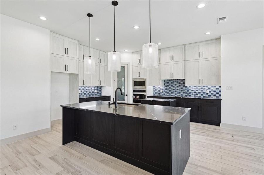 Kitchen featuring a center island with sink, sink, white cabinets, and light hardwood / wood-style floors