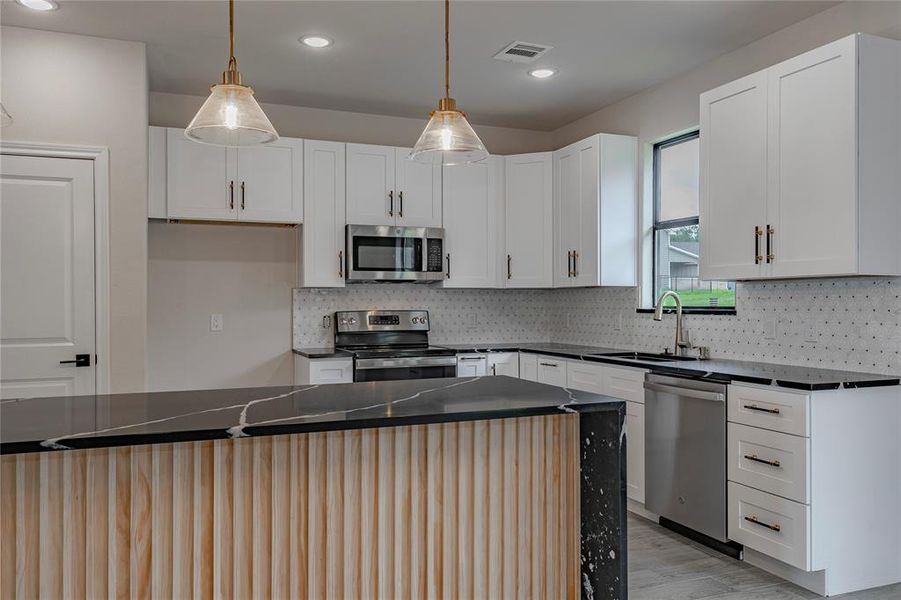 Kitchen featuring tasteful backsplash, light wood-type flooring, sink, white cabinets, and appliances with stainless steel finishes