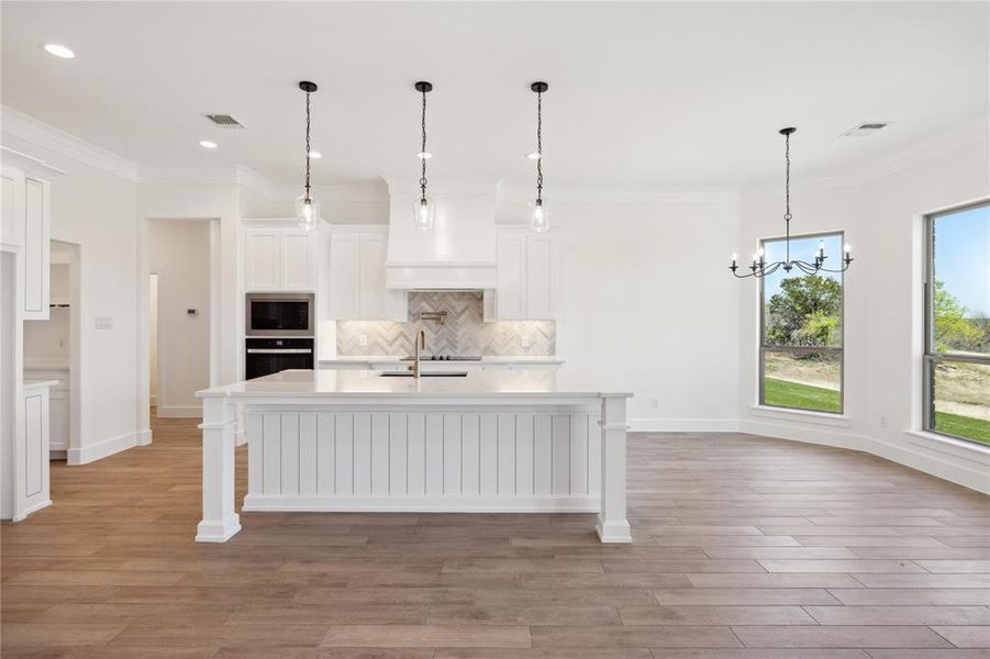 Kitchen featuring black oven, backsplash, an island with sink, pendant lighting, and sink